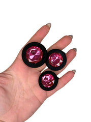 Three pink gemstones in black holders held in a hand against a white background