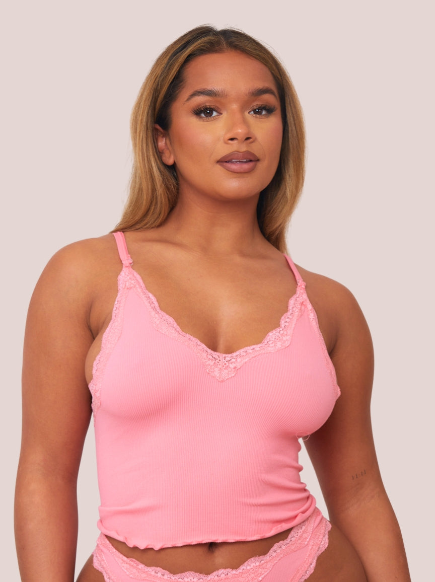 Woman wearing a pink lace-trimmed camisole against a plain background