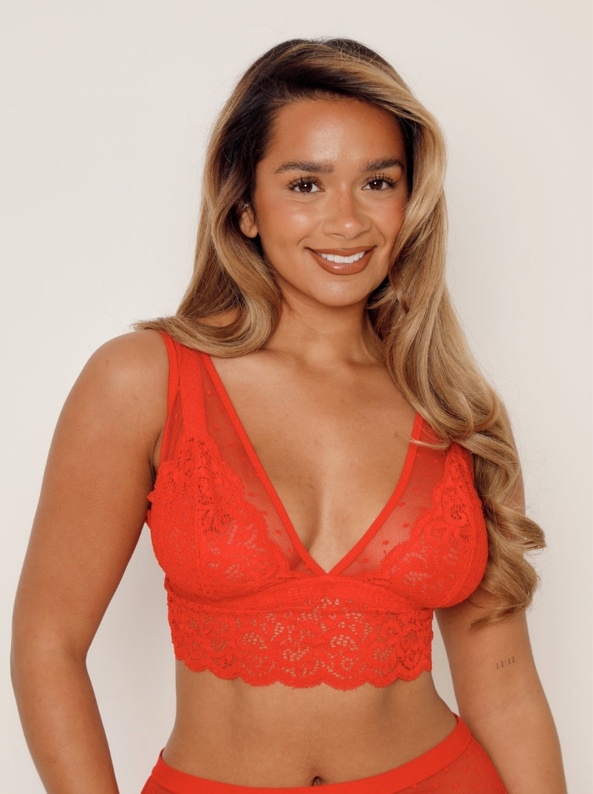 Woman wearing a red lace bralette against a plain background